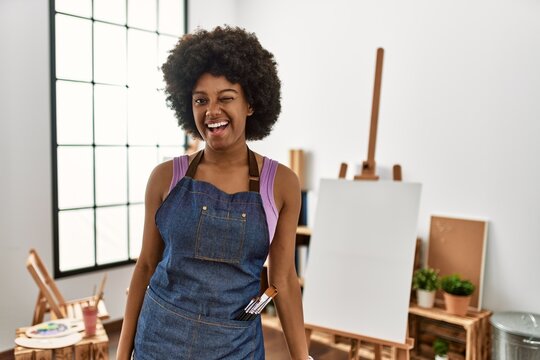 Young african american woman with afro hair at art studio winking looking at the camera with sexy expression, cheerful and happy face.
