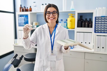 Young hispanic woman working at scientist laboratory with blood samples smiling and laughing hard out loud because funny crazy joke.