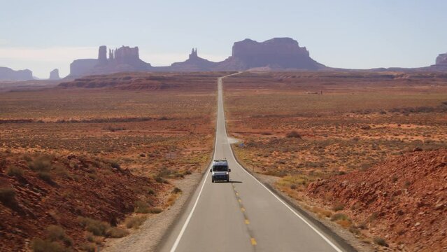 Aerial view of a RV on a road with Monument Valley peaks in the background - tracking, drone shot