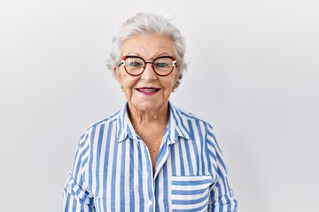 Senior woman with grey hair standing over white background with a happy and cool smile on face....