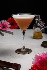 A freshly made French Martini cocktail, on a white backdrop and styled with bar equipment and pink and red flowers.