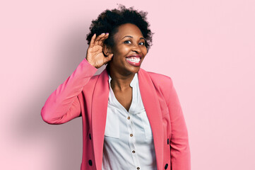 African american woman with afro hair wearing business jacket smiling with hand over ear listening an hearing to rumor or gossip. deafness concept.