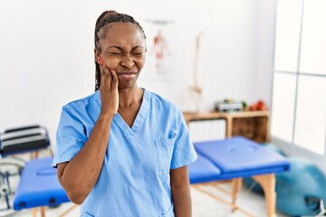 Black woman with braids working at pain recovery clinic touching mouth with hand with painful expression because of toothache or dental illness on teeth. dentist