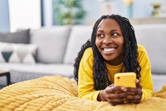 African american woman using smartphone lying on sofa at home