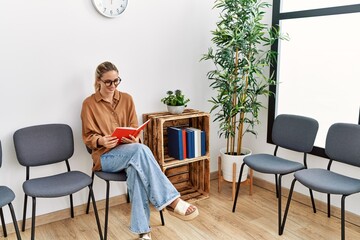 Young blonde woman smiling confident reading book at waiting room