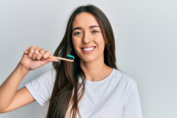Young hispanic girl holding toothbrush with toothpaste looking positive and happy standing and smiling with a confident smile showing teeth