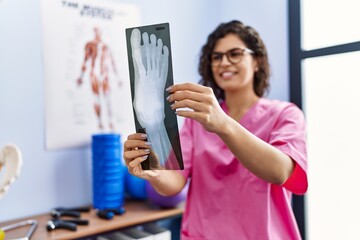 Young latin woman wearing physiotherapist uniform looking xray at clinic
