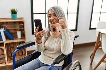 Middle age grey-haired woman having teleconsultation sitting on wheelchair at home