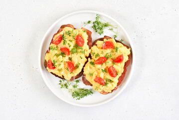 Scrambled eggs with microgreen, bacon and tomatoes on bread