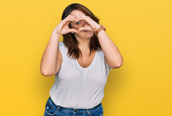 Young plus size woman wearing casual white t shirt doing heart shape with hand and fingers smiling looking through sign