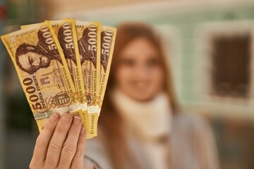 Young redhead girl smiling happy holding hungarian forint banknotes at the city.