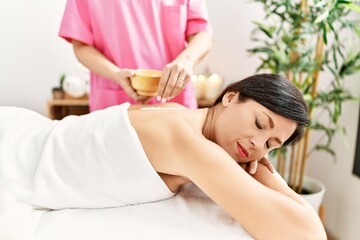 Middle age hispanic woman having salt back massage at beauty center