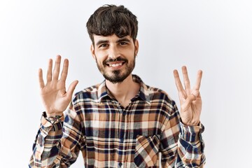 Hispanic man with beard standing over isolated background showing and pointing up with fingers number eight while smiling confident and happy.