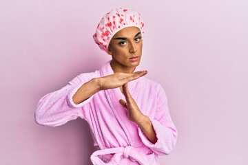 Hispanic man wearing make up wearing shower towel cap and bathrobe doing time out gesture with...