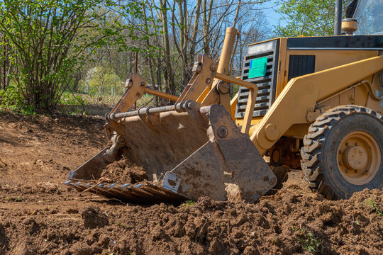 Clearing and leveling a private land plot. Yellow excavator driving earth in a wide bucket