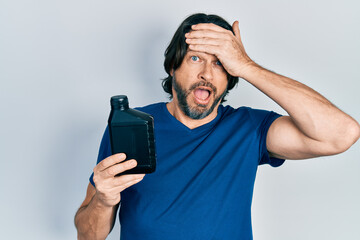 Middle age caucasian man holding motor oil bottle stressed and frustrated with hand on head,...