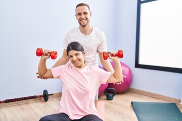 Fototapeta na wymiar Man and woman couple smiling confident training using dumbbells at sport center