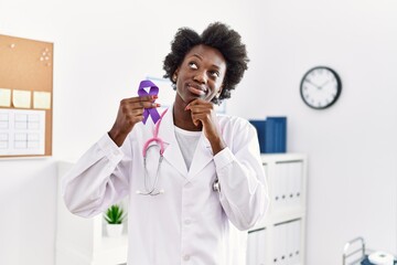 African doctor woman holding purple ribbon awareness at medical clinic serious face thinking about...