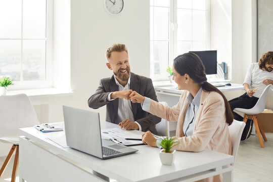 Business People Making Deal. Company Employees Greeting Each Other. Happy Businessman And Businesswoman Sitting At Office Desk Table With Notebook PC Fist Bumping After Job Well Done. Teamwork Concept