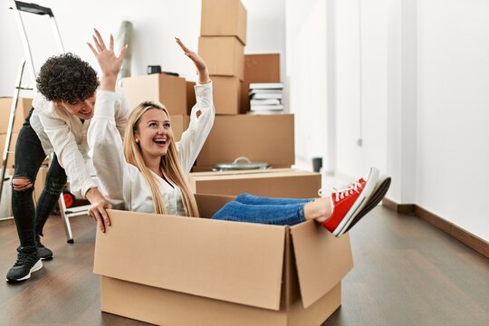 Young beautiful couple smiling happy playing using cardboard box as a car at new home.
