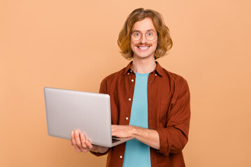 Portrait of handsome cheerful skilled trendy red-haired guy holding using laptop isolated over beige pastel color background