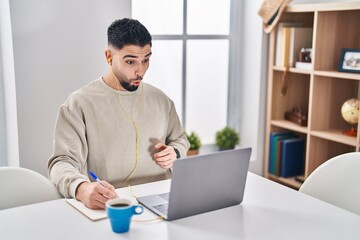 Fototapeta premium Young handsome man using computer laptop doing online call scared and amazed with open mouth for surprise, disbelief face