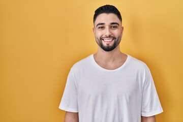 Young handsome man wearing casual t shirt over yellow background with a happy and cool smile on...