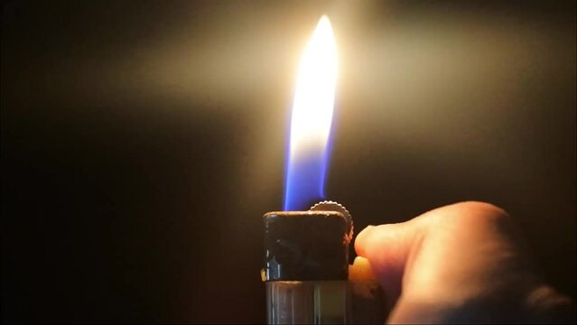 gas lighter videos. close-up fire from the lighter igniting in the hand in the dark on a black background. Man's hand with gas lighter.
