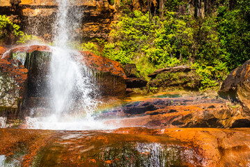 waterfall white streams falling from mountain top at yellow rocks with rainbow at morning