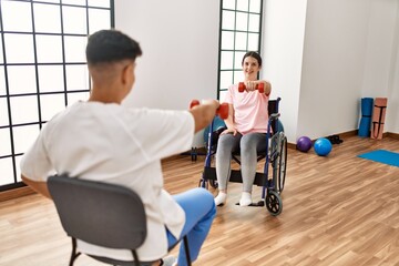 Young disabled woman sitting on wheelchair making mobility exercise using dumbbells at the clinic.
