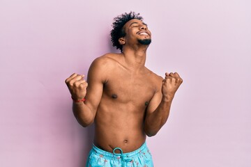 Fototapeta premium Young african american man with beard wearing swimsuit very happy and excited doing winner gesture with arms raised, smiling and screaming for success. celebration concept.