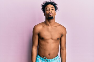 Fototapeta premium Young african american man with beard wearing swimsuit making fish face with lips, crazy and comical gesture. funny expression.