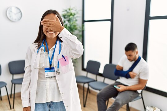Young asian doctor woman at waiting room with a man with a broken arm smiling and laughing with hand on face covering eyes for surprise. blind concept.