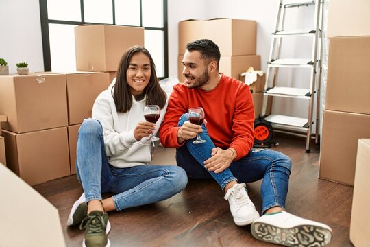 Young latin couple smiling happy toasting with red wine at new home