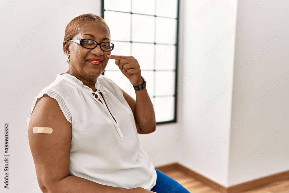 Poster mature hispanic woman getting vaccine showing arm with band aid pointing with hand finger to face an