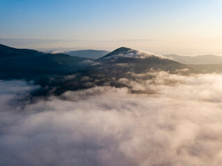 Flight over fog in Ukrainian Carpathians in summer. Mountains on the horizon. Aerial drone view.