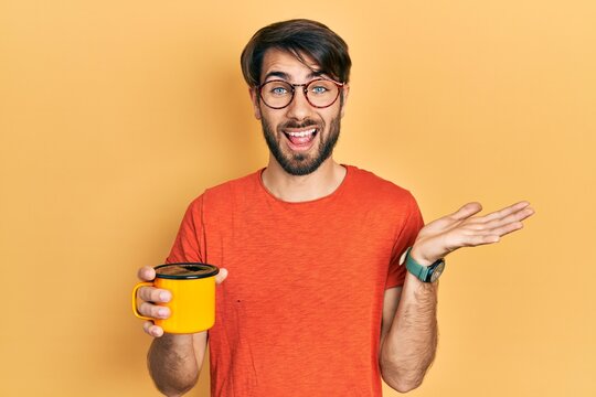 Young hispanic man drinking a cup of coffee celebrating achievement with happy smile and winner expression with raised hand