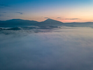 The rays of dawn over the fog in the Ukrainian Carpathians. Aerial drone view.