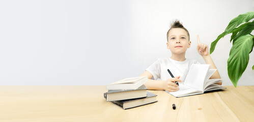 The boy writes in a notebook and looks up thoughtfully. Banner