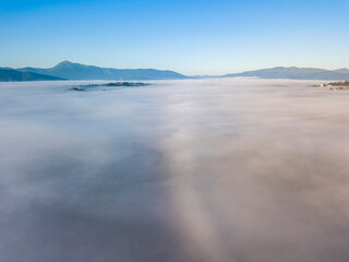 Flight over fog in Ukrainian Carpathians in summer. Mountains on the horizon. A thick layer of fog covers the mountains with a continuous carpet. Aerial drone view.