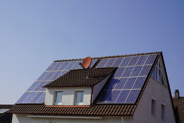 Dach von einem kleinen Wohnhaus mit Solar Modulen belegt. Der strahlend blaue Himmel verspricht...