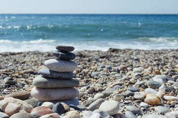 Fototapeta na wymiar Pyramid of sea pebbles on a sunny sandy beach. The concept of life 