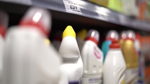A girl chooses detergents in a store. Her hand picks up a bottle of detergent.
