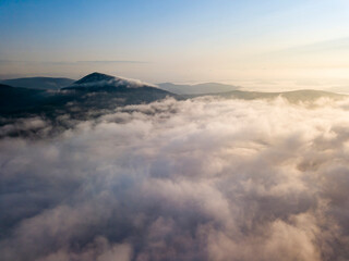 Flight over fog in Ukrainian Carpathians in summer. Mountains on the horizon. Aerial drone view.