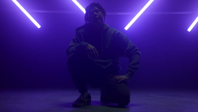 Cool dancer guy sitting posing confidently on dance floor in night club lights.