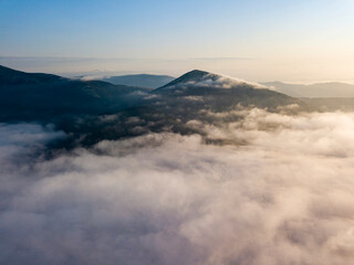 Flight over fog in Ukrainian Carpathians in summer. Mountains on the horizon. Aerial drone view.