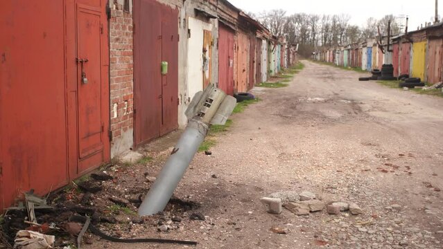 Close-up view 4k stock video footage of real unexploded military missile, torpedo or shell stuck in ground near doors of garages outdoors. Moments of dreadful war of Russia against Ukraine in 2022