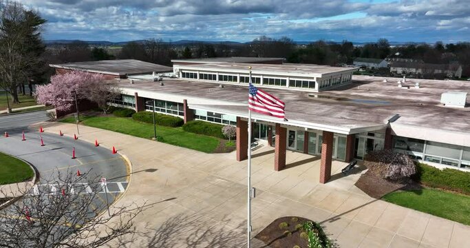 Front entrance of American school building. Dramatic sunny to cloudy lighting. USA flag and flag pole at front entrance.