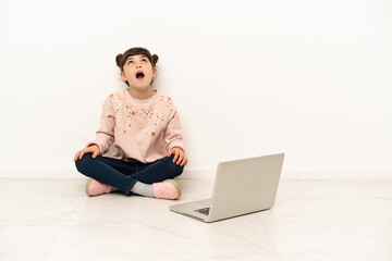 Little girl with a laptop sitting on the floor looking up and with surprised expression