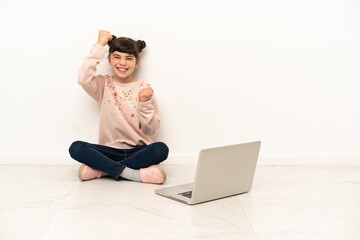 Little girl with a laptop sitting on the floor celebrating a victory